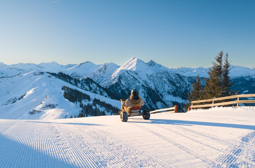 Person fährt Schneekart auf frisch präparierter Piste mit Blick auf verschneite Berge bei Sonnenschein. | © Dorfgasteiner Bergbahnen AG