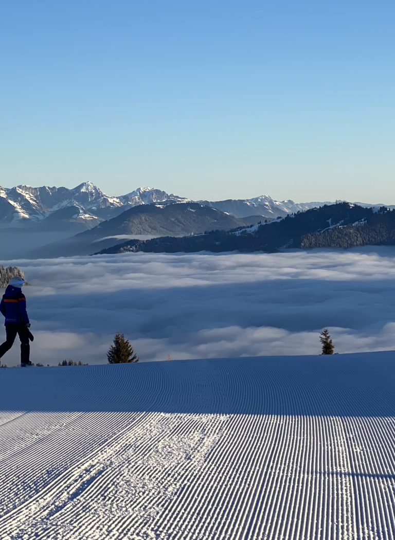 Person stands on freshly groomed ski slope overlooking foggy valley and peaks | © Großarler Bergbahnen GmbH & Co KG