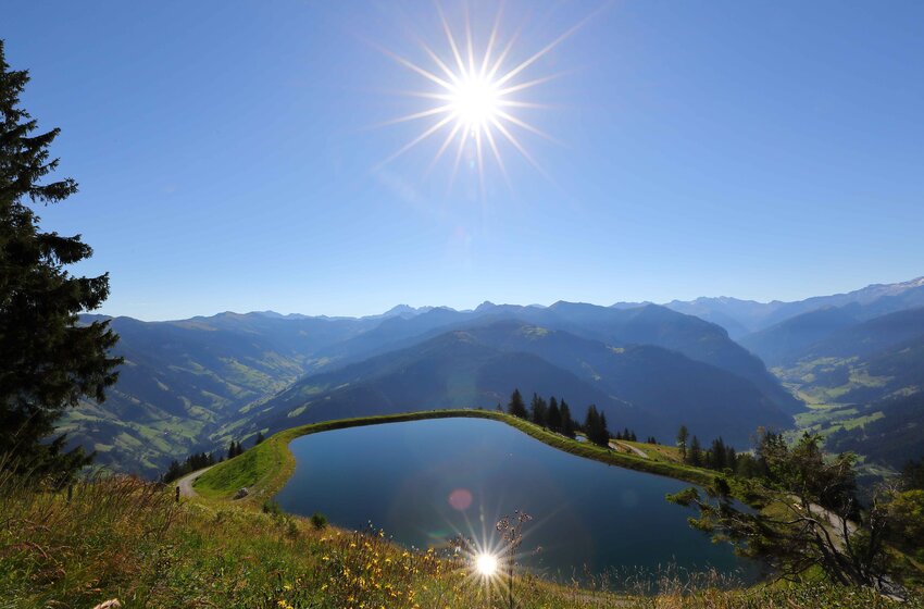  Mountain lake with sun reflection above Großarltal, overlooking green hills and distant alpine peaks | © Grossarler Bergbahnen GmbH & Co KG