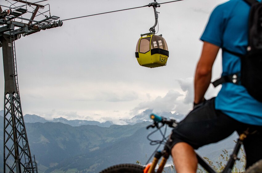 Mountainbiker von hinten vor gelber Nostalgie-Gondel der Großarlbahn mit bewölktem Himmel und Alpenkulisse | © Grossarler Bergbahnen GmbH & Co KG