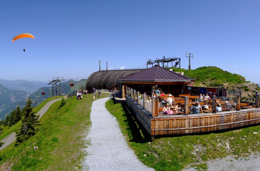 Panorama with paragliders, mountain station and sun terrace in summer in Großarl | © Grossarler Bergbahnen GmbH & Co KG Paragliders over Großarltal near mountain station with visitors on sun terrace and panoramic view | © Grossarler Bergbahnen GmbH & Co KG