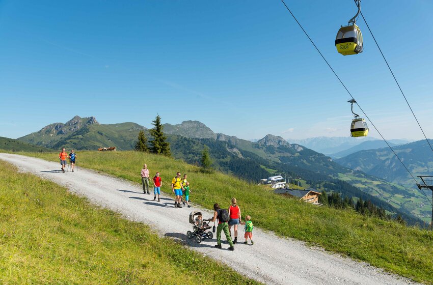 Hikers with children and stroller on alpine path in Großarl, yellow gondolas of the panorama lift in background | © Grossarler Bergbahnen GmbH & Co KG