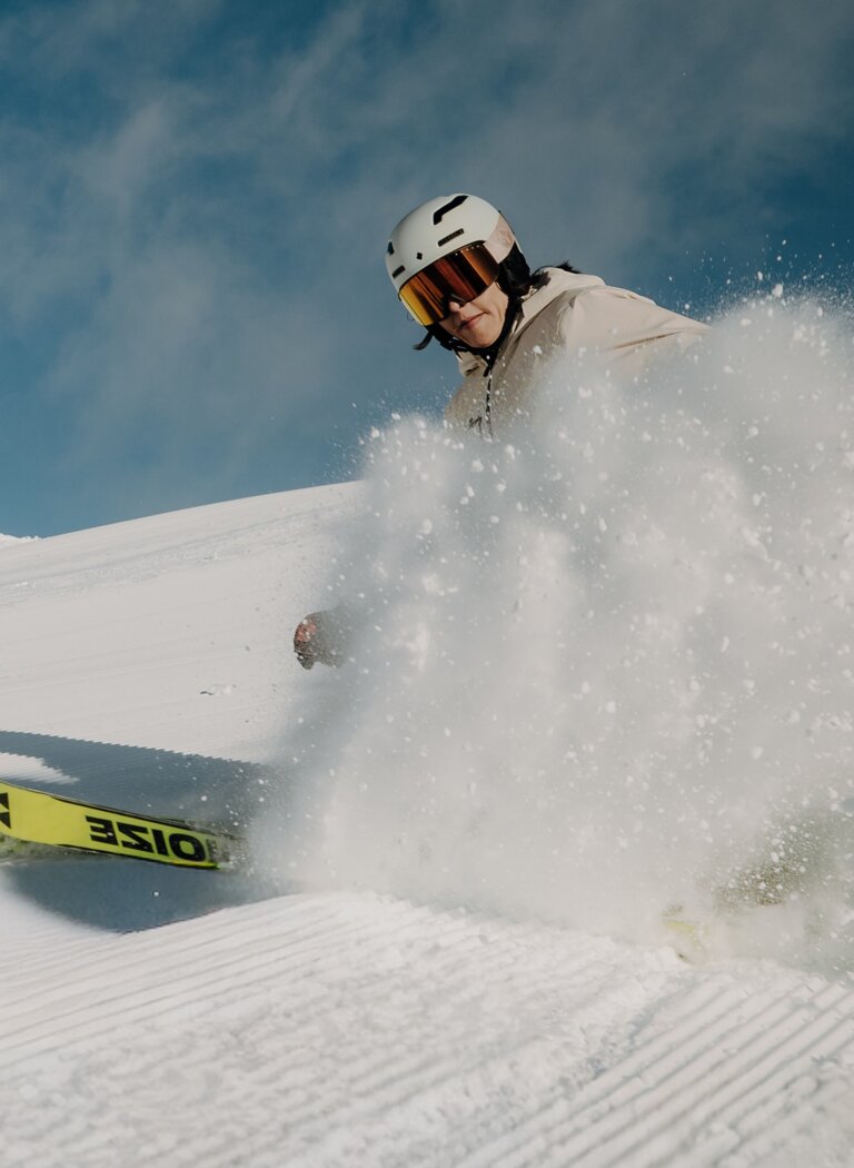 A skier carves a turn on a freshly groomed piste, spraying snow beneath a clear blue winter sky. | © Elisabeth Toferer