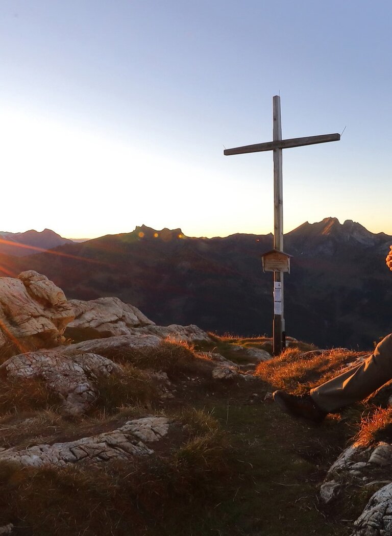 Wanderer sitzt beim Gipfelkreuz im Großarltal und blickt in den Sonnenuntergang. | © Tourismusverband Großarltal
