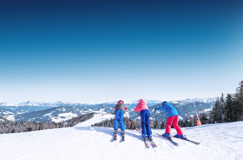 Three kids skiing downhill in Ski amadé family area | © Ski amadé GmbH Three children at the top of a ski slope, ready to go downhill with snowy mountains in the background. | © Ski amadé GmbH